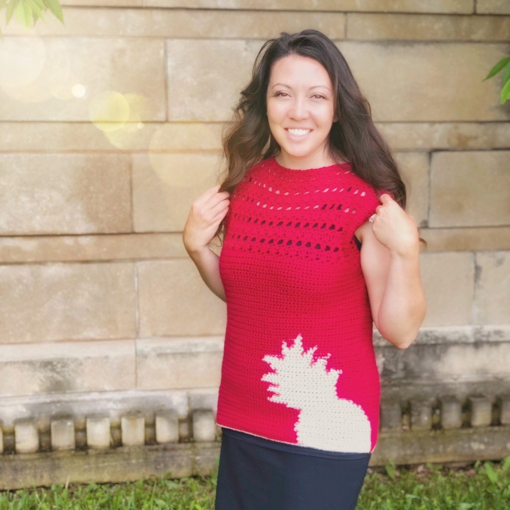 A red crochet top with a cream pineapple in the bottom corner and open stitching at the yoke-An original design by The Plush Pineapple