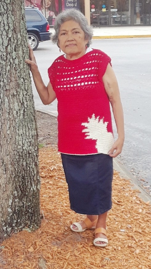 Red crochet top with cream pineapple color work in the bottom right corner with a lacy, open yoke and cap sleeves shown in use